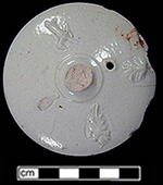 Lid to teapot or coffee pot with sprig molded decorations.&nbsp;The slight shadow created by the metal sprig mold can be seen around the sprigged element at the lower right and in the detail shot.&nbsp;The unglazed area at the lower left is where another sprigged element detached from the lid., Vessel 224, recovered from 1740s level within a well filled c. 1720s-1750s - 18PR175.
